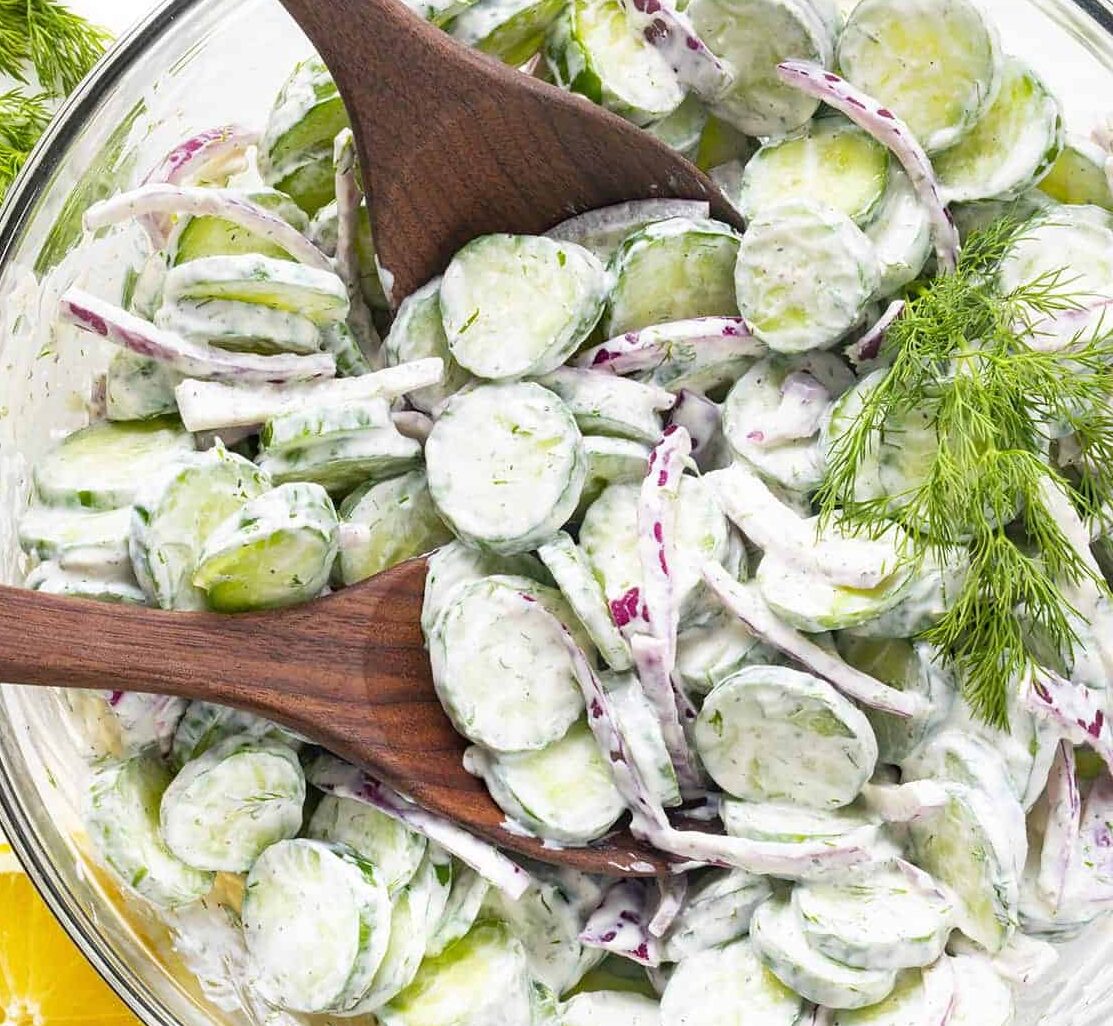 A salad with cucumbers and dressing with wooden spoons in the bowl